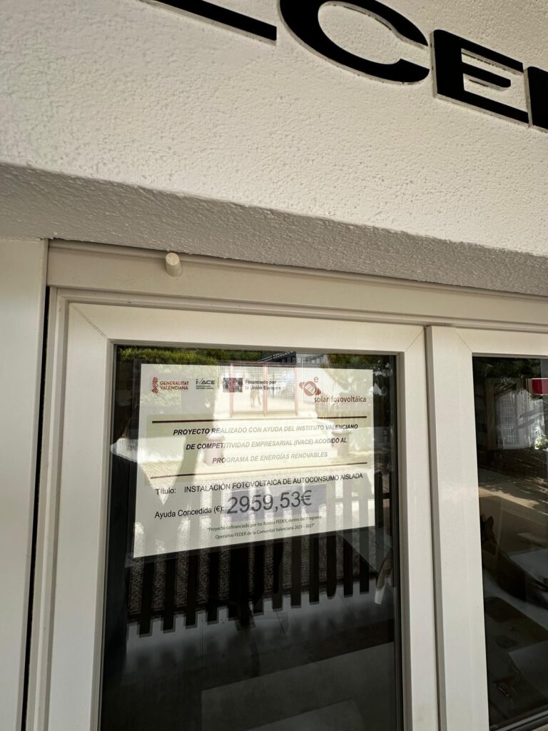Door with a posted document visible in the glass, showing logos and text about a photovoltaic project (in Spanish).