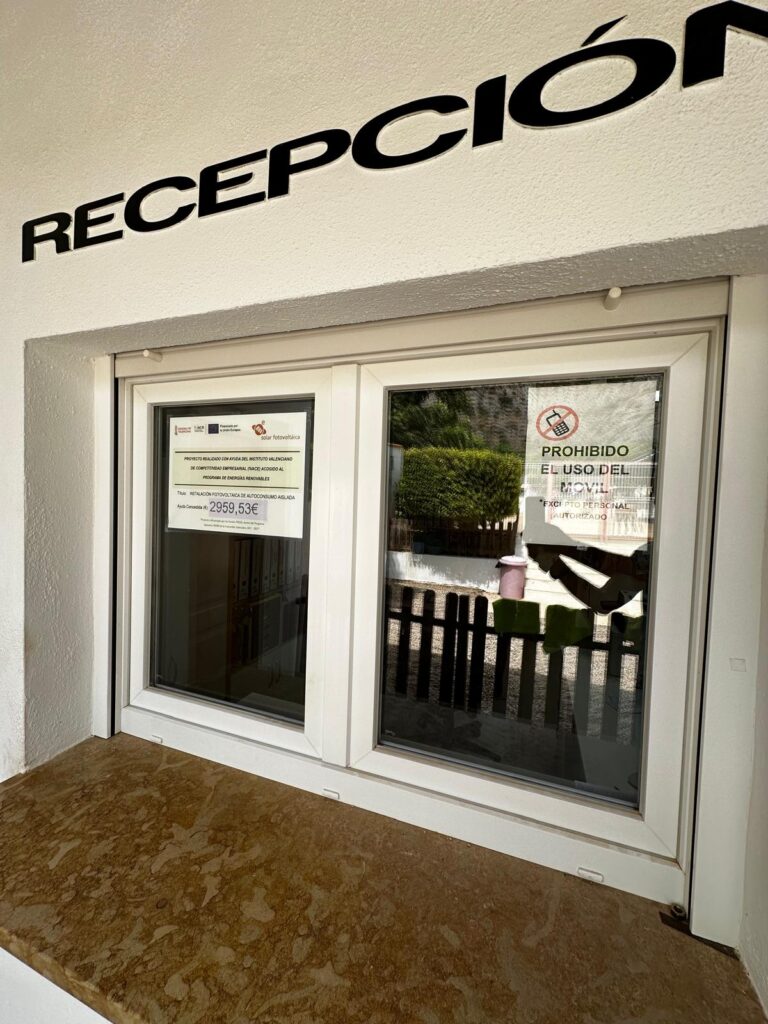 Reception area with a large 'RECEPCIÓN' sign above a double glass door and posted notices on the windows.